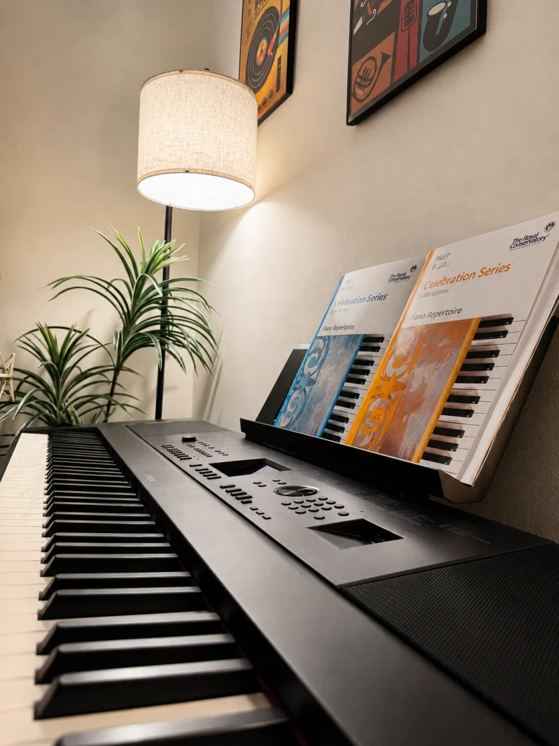 Digital piano with repertoire books, a floor lamp, and plants. Digital piano with repertoire books, a floor lamp, and plants.